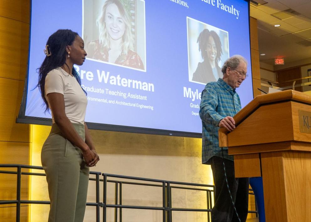 Myleah Brewer stands on stage with Dan Bernstein speaks at a podium.
